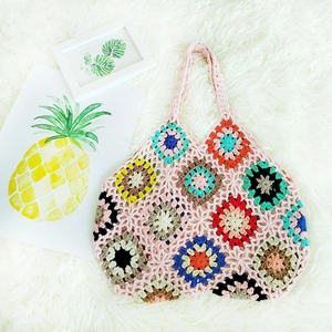 Detail of handmade crochet handbag with colorful granny square patterns and pink handles