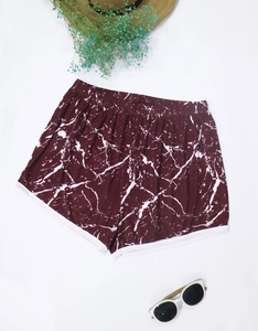 Flat lay of burgundy marble print beach shorts with white trim and summer accessories