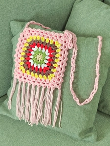 Macro shot of handmade crochet crossbody bag with pink fringes and bohemian floral patterns
