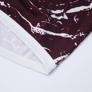 Close-up of double-stitched white piping on burgundy marble print beach shorts fabric