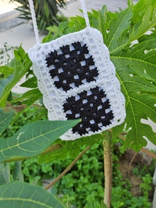 Detail of handmade crochet phone bag featuring black and white granny square patterns