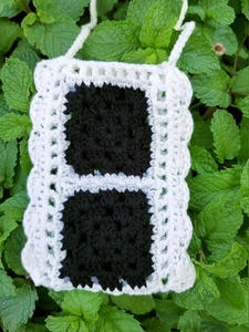 Macro shot of handmade crochet phone bag featuring black motifs and white lace borders