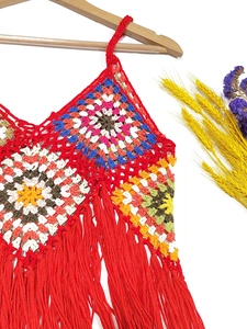 Macro detail of Bohemian handmade crochet top with colorful floral patterns and red fringe