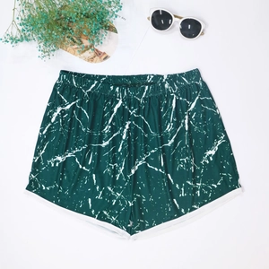 Detailed flat lay of green marble print beach shorts with white piping and summer props
