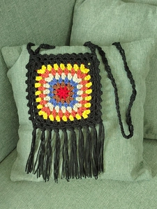 Detail of colorful handmade crochet grandmother square bag with long black tassels and fringe