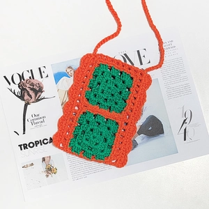 Macro shot of orange handmade crochet phone bag with green square pattern on Vogue magazine