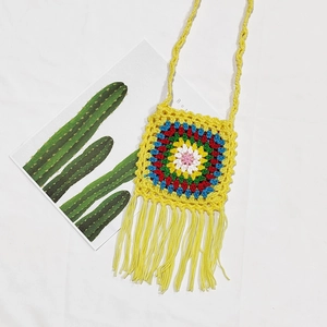 Close-up of handmade yellow crochet crossbody bag with floral pattern and long fringe