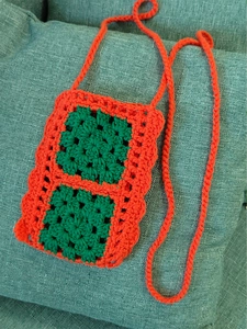 Close-up of handmade crochet phone bag with green granny square and orange strap