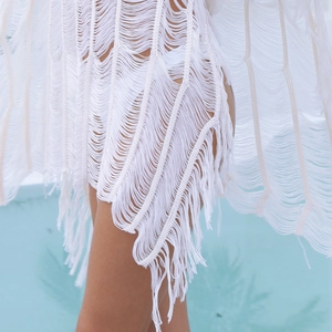 Detailed view of white crochet beach cover-up featuring elegant fringe and woven texture