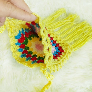 Detail view of handmade crochet bag showing yellow tassels and colorful interior floral patterns