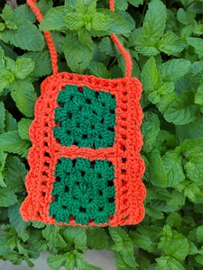 Detail of a handmade crochet crossbody bag with orange and green granny square design