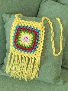 Macro detail of yellow handmade crochet granny square bag with colorful pattern and fringe