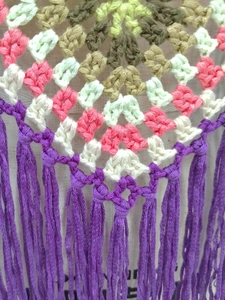 Detail of handmade crochet patchwork top with bohemian colorful patterns and purple fringes