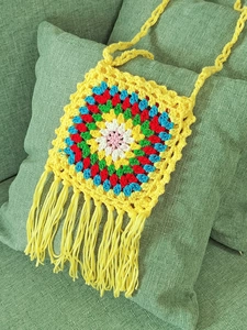 Close-up of handmade crochet bag with colorful floral pattern and yellow tassel detail