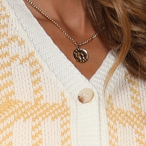 Gros plan d'un collier pièce dorée avec texture martelée sur un pull à carreaux