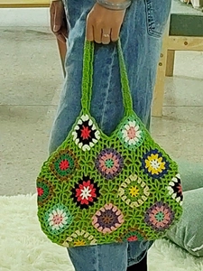 Close-up of handmade crochet tote bag featuring multi-colored floral patchwork and green handles
