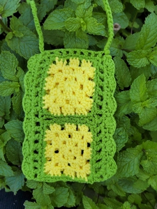Handmade crochet crossbody bag featuring yellow floral patterns and green woven strap