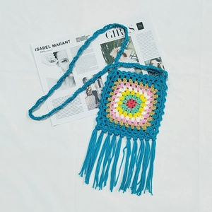 Macro shot of turquoise crochet shoulder bag with colorful boho pattern and long fringes