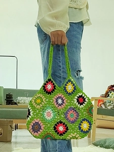 Detail of green hand-crocheted tote bag with colorful sunflower patterns and wide handles