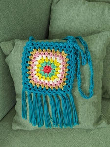 Detail of colorful hand-crocheted crossbody bag with sunflower pattern and blue tassels