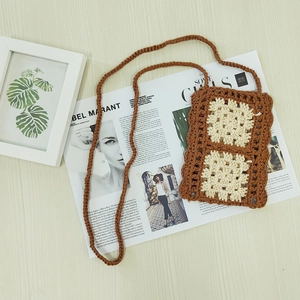 Hand-woven bohemian phone bag with crochet flower patterns on light wood background