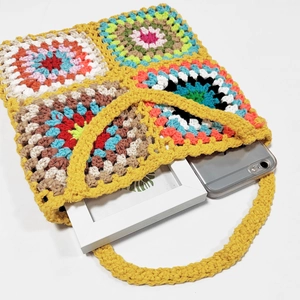 Macro shot of colorful crochet granny square bag with yellow handles and phone for scale
