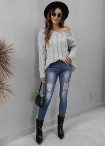 Outdoor street style shot of a woman in a grey cable knit sweater and ripped jeans