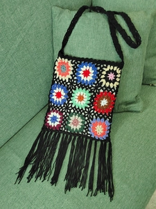 Close-up of handmade crochet granny square bag with colorful patterns and black tassels
