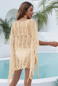 Detailed close-up of cream knit beach cover-up with fringe hem and hollow-out crochet design