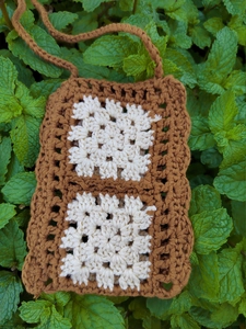 Macro detail of hand-woven crochet bag featuring brown frames and white granny square motifs