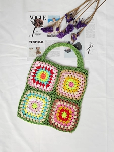 Macro view of a colorful handmade granny square crochet handbag on a white fabric base