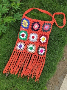 Close-up of handmade granny square crochet crossbody bag with vibrant orange tassels