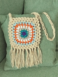 Detail of bohemian handmade crochet granny square crossbody bag with long fringes on a sofa