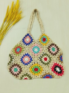 Close-up of handmade crochet tote bag with colorful flower patterns on wood background