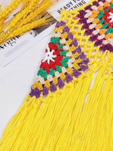 Detailed macro of handmade crochet top featuring colorful square patterns and yellow tassels