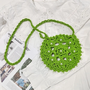 Close-up of handmade green crochet round bag with white floral pearls on a lace shirt