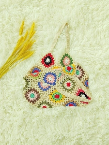 Detail of colorful crochet granny square handbag on white plush rug with dried wheat