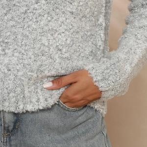 Détail d'un pull gris en maille bouclée avec poignets côtelés et jean bleu délavé