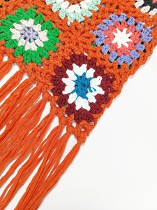 Close-up of colorful handmade granny square crochet bag with orange fringe details