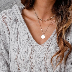 Detail of layered gold chain necklaces with coin pendant over grey cable knit sweater