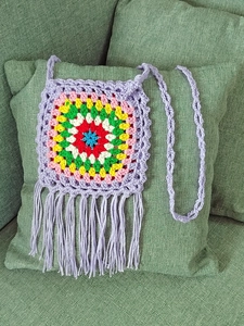 Detail of handmade crochet shoulder bag featuring colorful granny square and long fringes