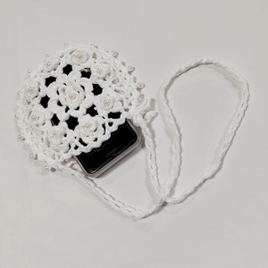 Detail of white crochet phone bag with 3D floral textures and pearl accents