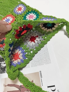 Macro detail of a green handmade crochet tote bag featuring colorful floral knit patterns