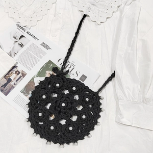 Detail of hand-crocheted black crossbody bag with white pearls on a lace background