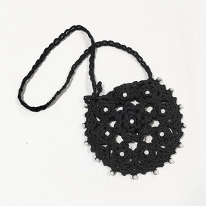 Detail of hand-crocheted black round bag with intricate hollow patterns and white pearls