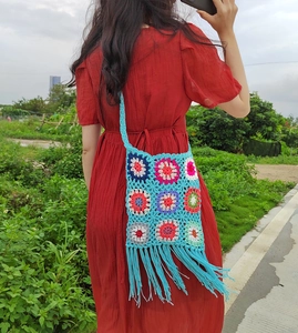 Detail of colorful crochet hobo bag with sunflower squares and long tassels on red dress