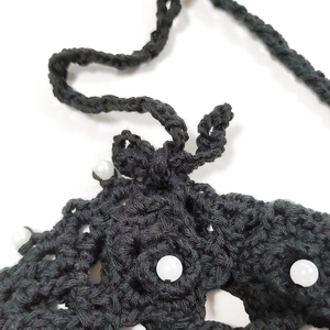 Detail of black crochet ethnic crossbody bag with hollow weave pattern and white pearls