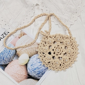 Detail of hand-crocheted beige crossbody bag with floral hollow pattern and white pearls