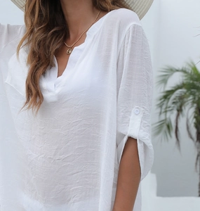 Détail de la tunique de plage blanche à col en V avec tissu texturé et manches boutonnées