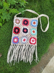 Detailed close-up of handmade crochet bag featuring colorful floral patches and long tassels